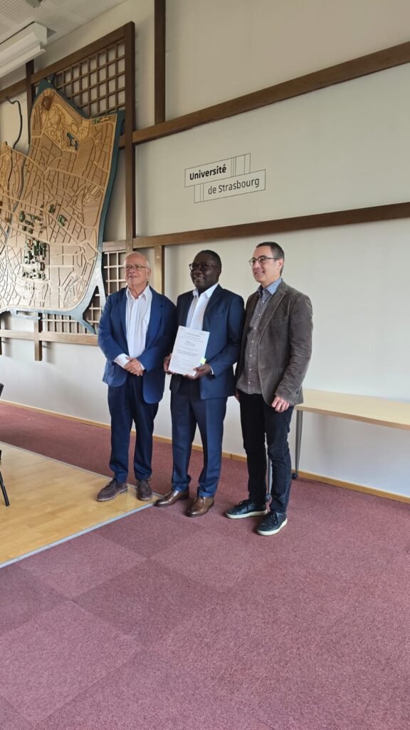 Fr Landry N’nang Ekomie holding his thesis between two members of the jury, University of Strasbourg