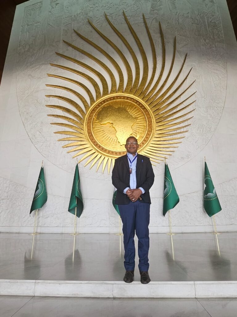 Padre Mwania chini ya nembo ya jua linalong'aa katika ukumbi mkuu wa makao makuu ya Umoja wa Afrika.