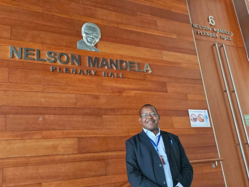 Padre Mwania kwenye mlango wa Ukumbi wa Mikutano Mikuu wa Nelson Mandela, makao makuu ya Umoja wa Afrika.