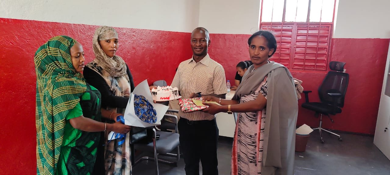 School staff presenting flowers, cake and a gift in the staff room